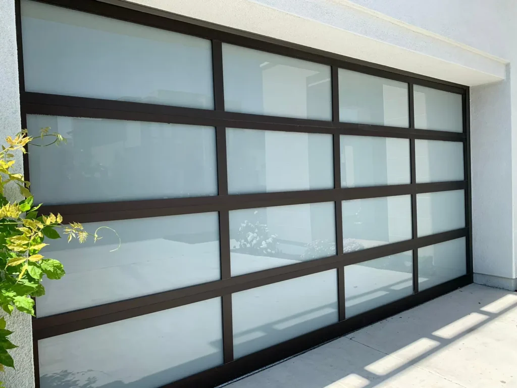 A close-up view of a very large, contemporary garage door or wall of windows, featuring dark brown or black horizontal and vertical frames with large, rectangular frosted glass panels.