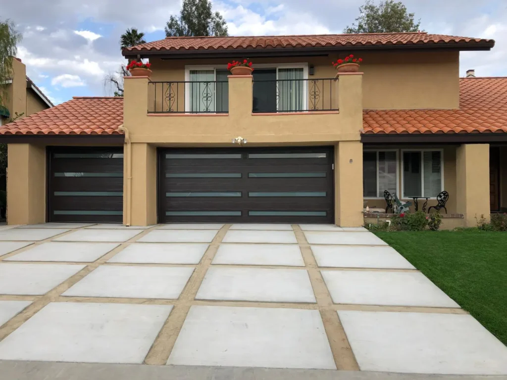 A two-story Spanish-style house with a terra cotta tile roof and a modern dark brown sectional garage door